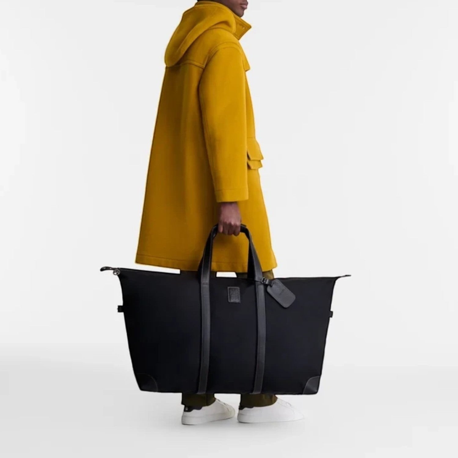 Lieblingstasche Longchamp Boxford black canvas travel bag with leather trim held by a man in a yellow coat