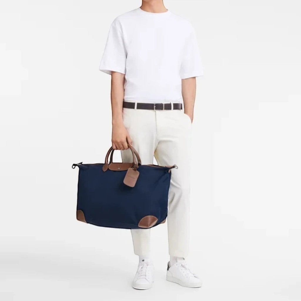 A man holding a navy blue Longchamp Boxford travel bag with brown leather details from Lieblingstasche