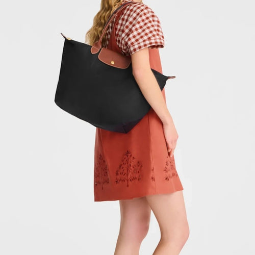 Lieblingstasche Longchamp Le Pliage large black shoulder bag with brown leather trim worn by a woman in a dress