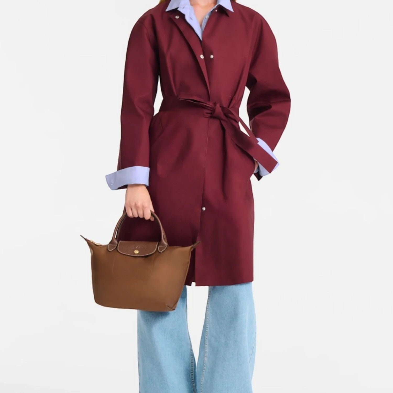 Model holding a brown Longchamp Le Pliage S handbag, wearing a burgundy trench coat and wide-leg jeans by Lieblingstasche