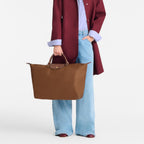 Lieblingstasche Longchamp Le Pliage large brown travel bag held by a blonde woman in a burgundy coat and blue jeans