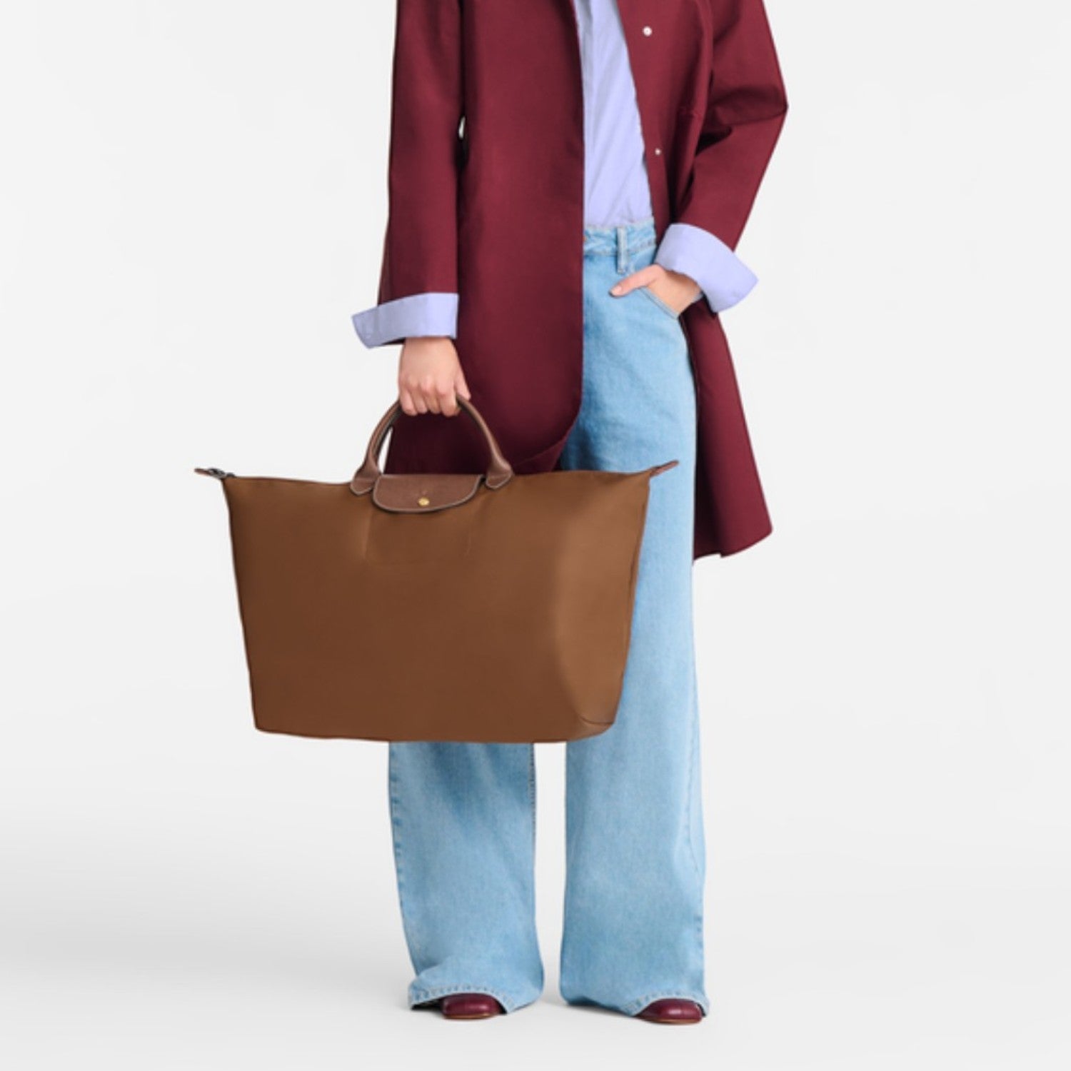 Lieblingstasche Longchamp Le Pliage large brown travel bag held by a blonde woman in a burgundy coat and blue jeans