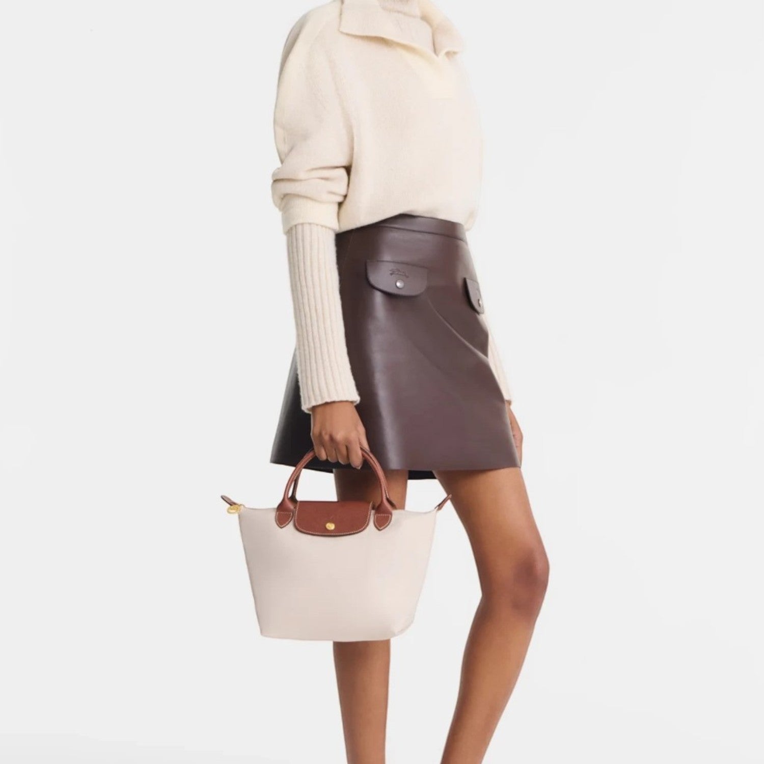 Model holding a beige and brown Lieblingstasche Longchamp Le Pliage small handbag with leather trim