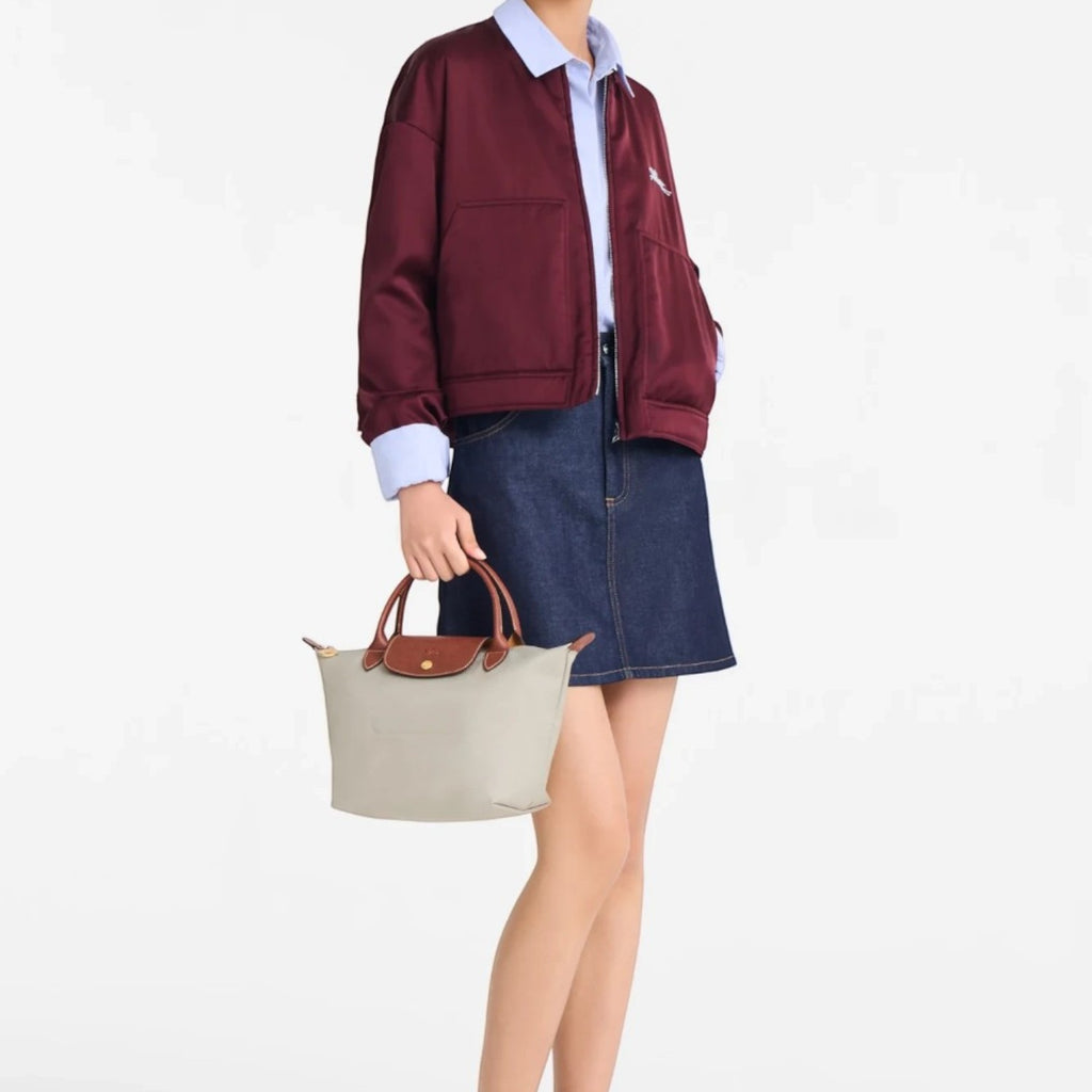 Model holding a beige Longchamp Le Pliage small handbag with brown leather handles, styled with a casual outfit.