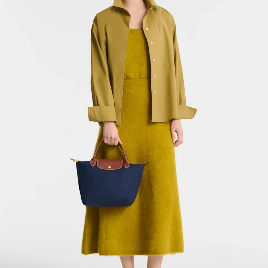 Lieblingstasche Longchamp Le Pliage small navy blue handbag with brown leather handles held by a model in yellow