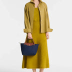 Lieblingstasche Longchamp Le Pliage small navy blue handbag with brown leather handles held by a model in yellow
