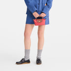 Model holding a small red Longchamp Le Pliage Pochette with brown leather trim, wearing a blue jacket and skirt.