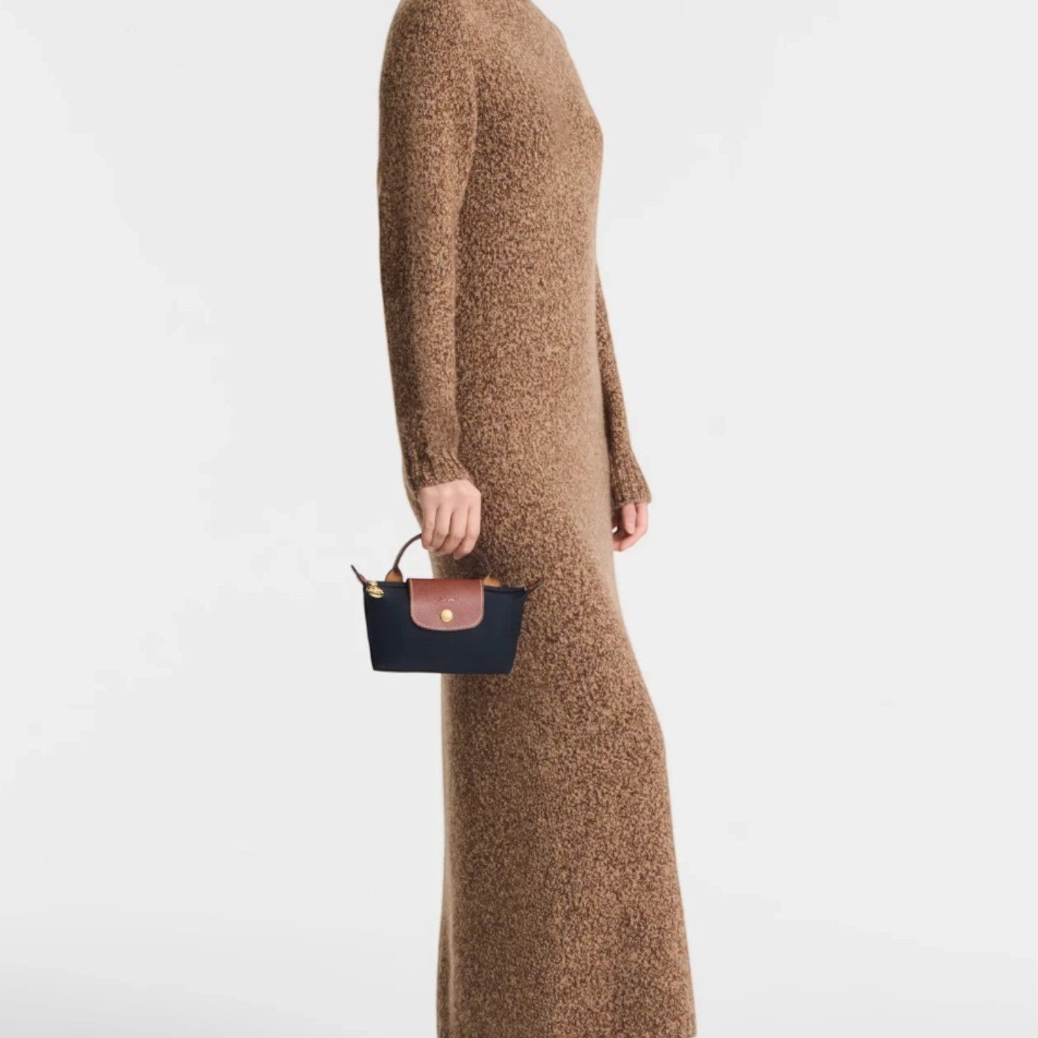 Lieblingstasche Longchamp Le Pliage Pochette in navy blue with brown leather trim held by a model in a brown dress