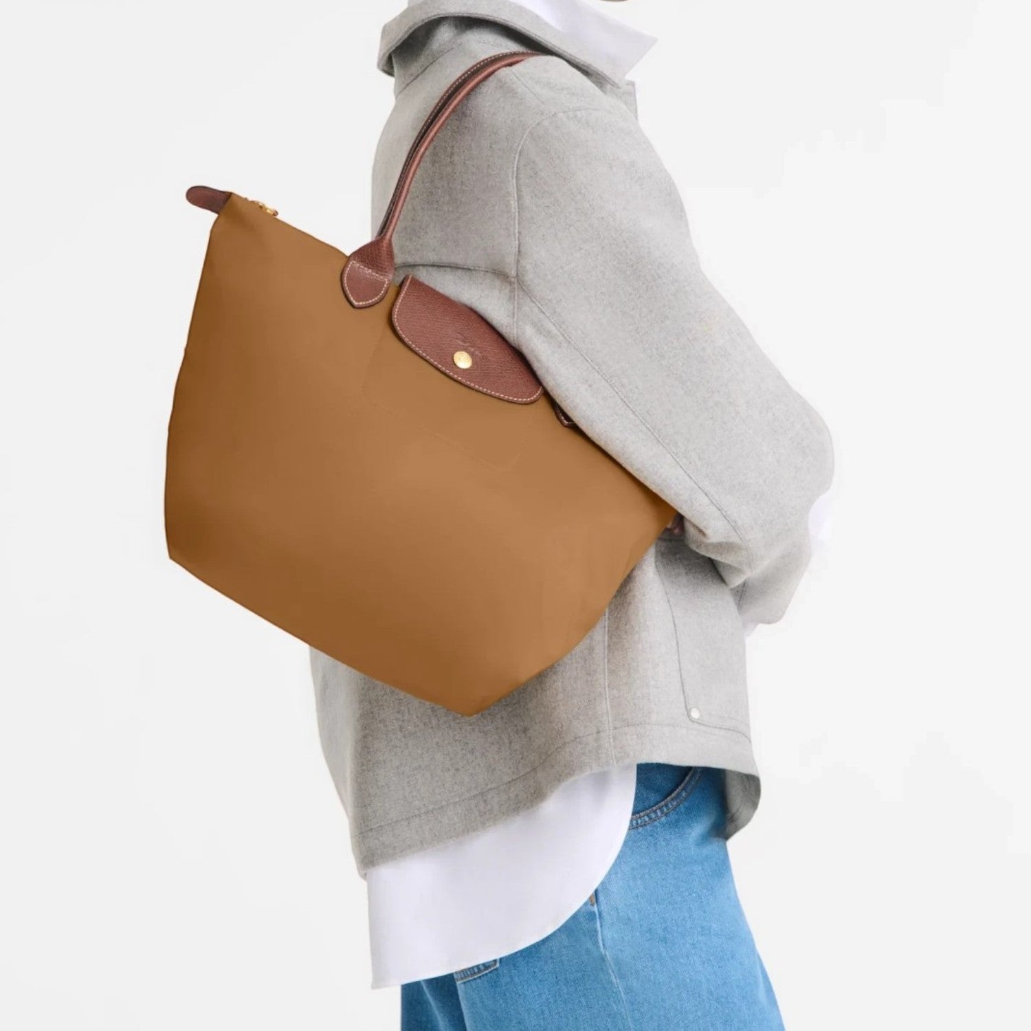 Model wearing a brown Lieblingstasche Longchamp Le Pliage shoulder bag with leather handles on a white background
