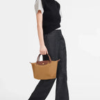 Model carrying a brown Lieblingstasche Longchamp Le Pliage small handbag with leather handles against a white background