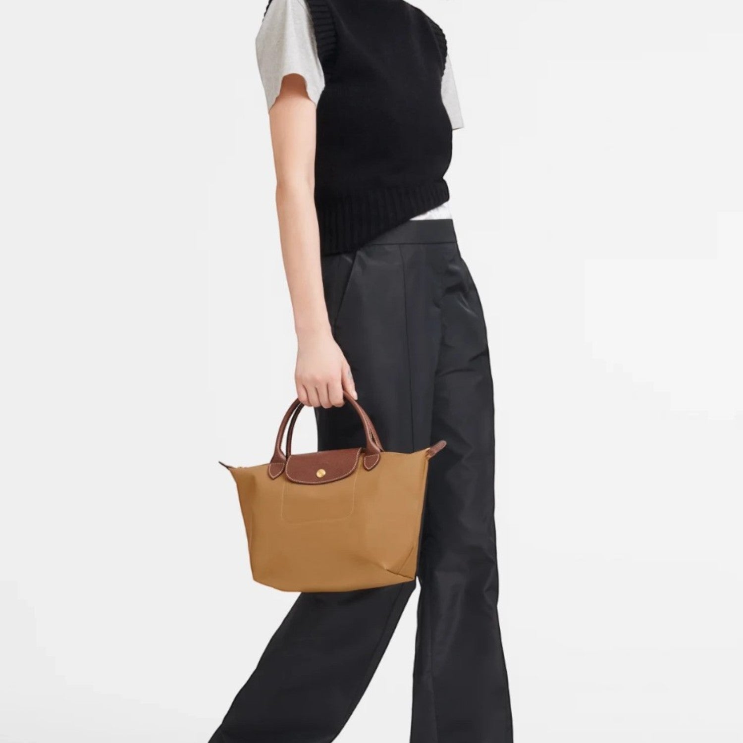 Model carrying a brown Lieblingstasche Longchamp Le Pliage small handbag with leather handles against a white background