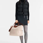 A model from Lieblingstasche wearing a black vest and holding a beige Longchamp Le Pliage travel bag with brown trim.