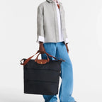 Model carrying a black Longchamp Le Pliage travel bag from Lieblingstasche with brown leather handles and strap
