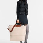 Model holding a beige Lieblingstasche Longchamp Le Pliage travel bag with brown leather handles and shoulder strap
