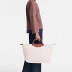 Model holding a large light pink Lieblingstasche Longchamp Le Pliage travel bag with brown leather handles