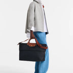 Model carrying a black Lieblingstasche Longchamp Le Pliage travel bag with brown leather handles and trim