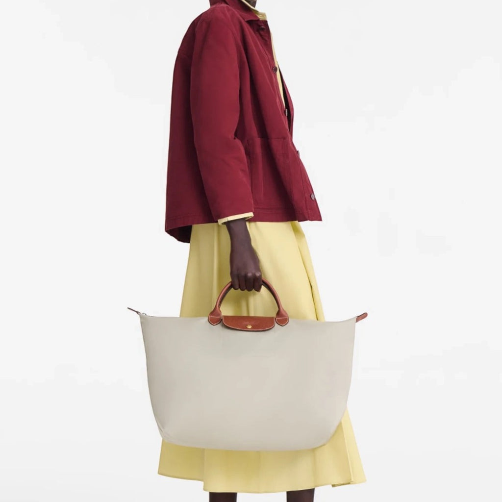 Model holding a beige Longchamp Le Pliage large travel bag with brown leather handles, Lieblingstasche collection.