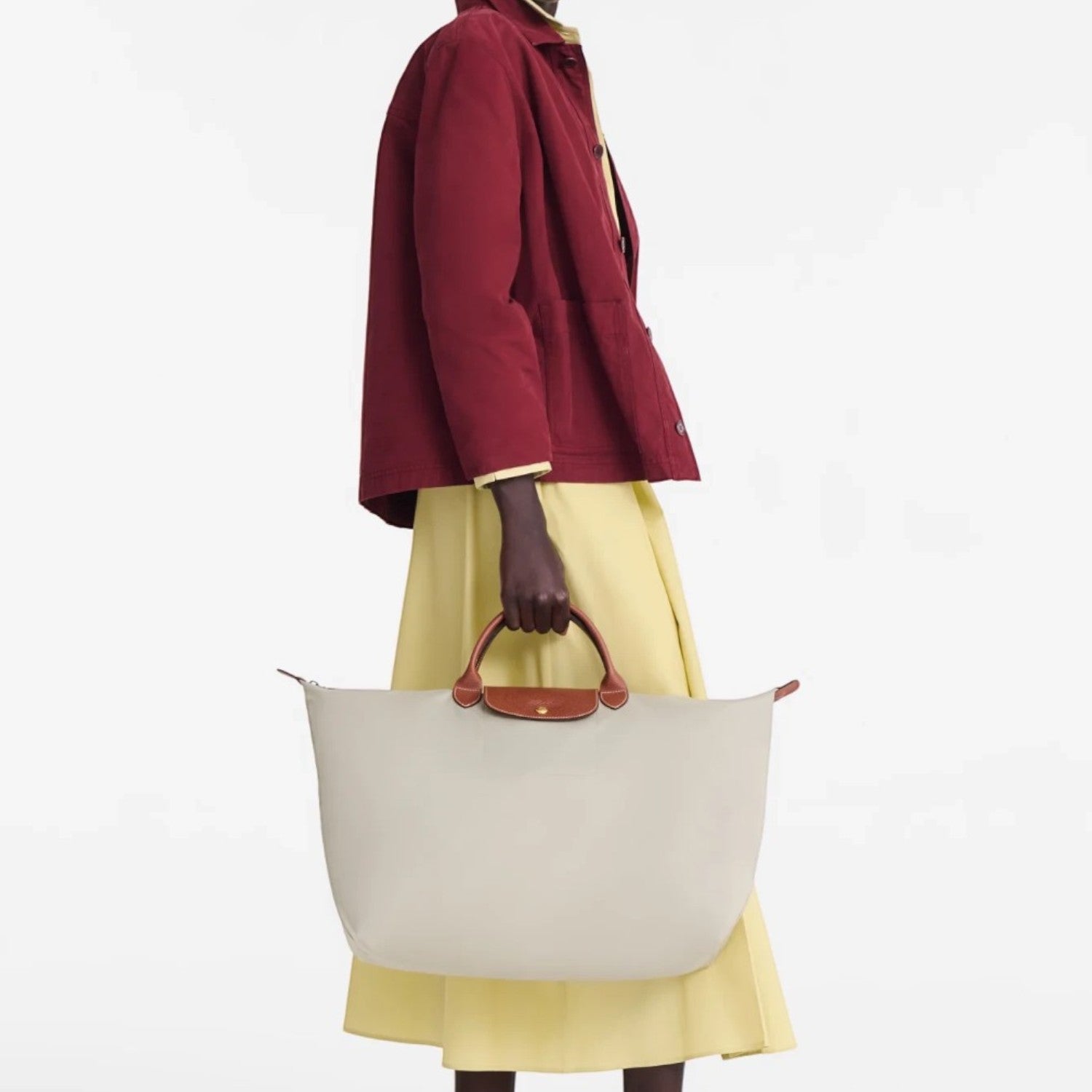 Model holding a beige Longchamp Le Pliage large travel bag with brown leather handles, Lieblingstasche collection.