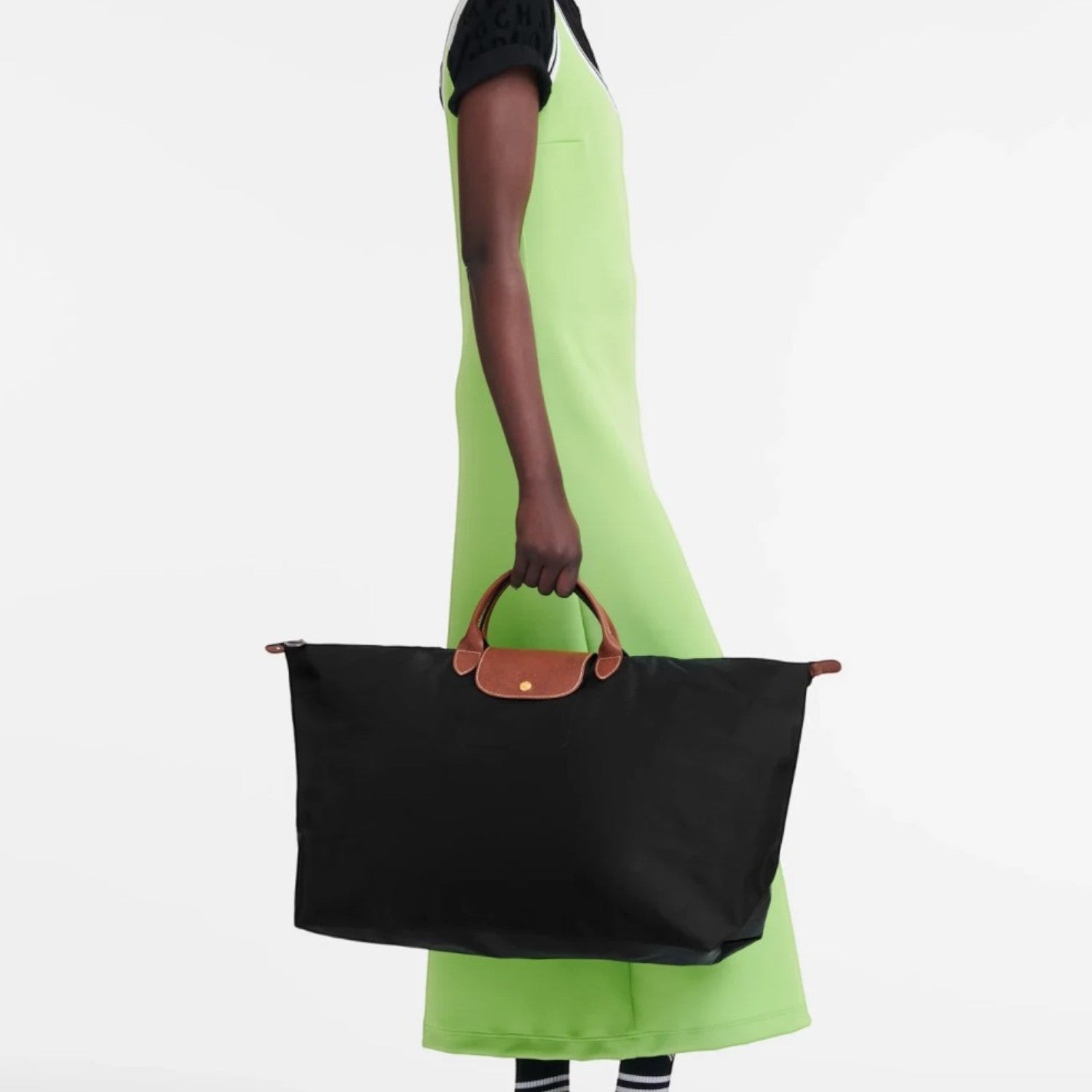 Model holding a black Longchamp Le Pliage large travel bag with brown leather handles against a white background