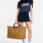 Lieblingstasche Longchamp Le Pliage XL travel bag in brown nylon with leather handles held by a model in sporty attire