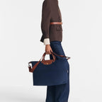 Model carrying a navy blue Longchamp Le Pliage travel bag with brown leather handles by Lieblingstasche