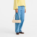 Lieblingstasche Looong Schultertasche S in beige, a sleek minimalist shoulder bag held by a model in yellow top