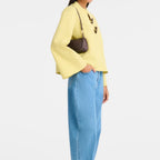Model wearing a Lieblingstasche Looong Schultertasche S in dark brown, styled with a yellow top and blue jeans.