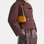 Model wearing a Lieblingstasche Looong Schultertasche S in mustard yellow, styled with a brown jacket and trousers.