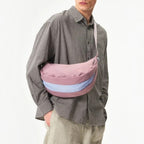 Lieblingstasche mauve and light blue crescent sling bag worn crossbody by a man in a plaid shirt and cap