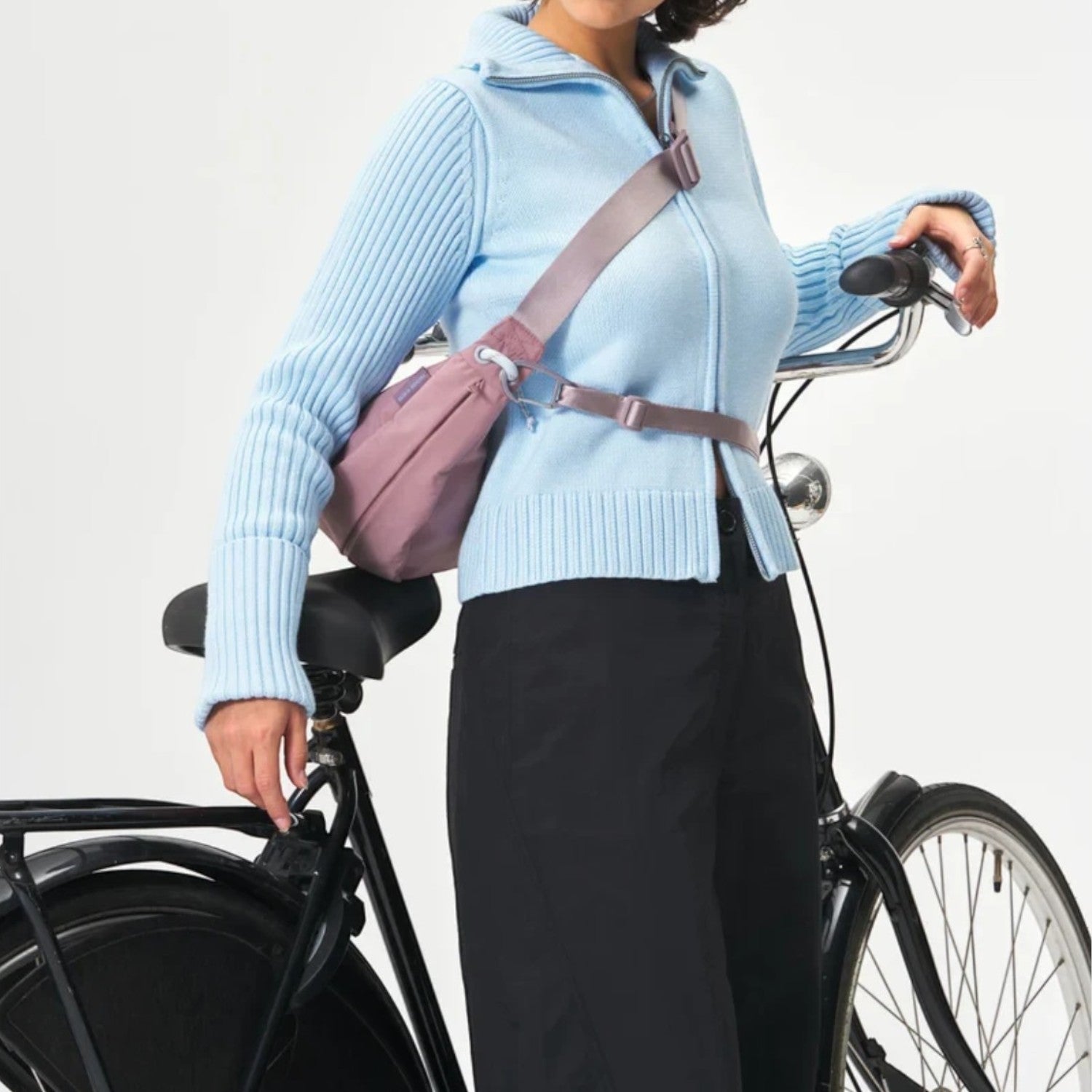 A woman wearing a mauve Lieblingstasche sling bag across her chest while standing next to a bicycle.