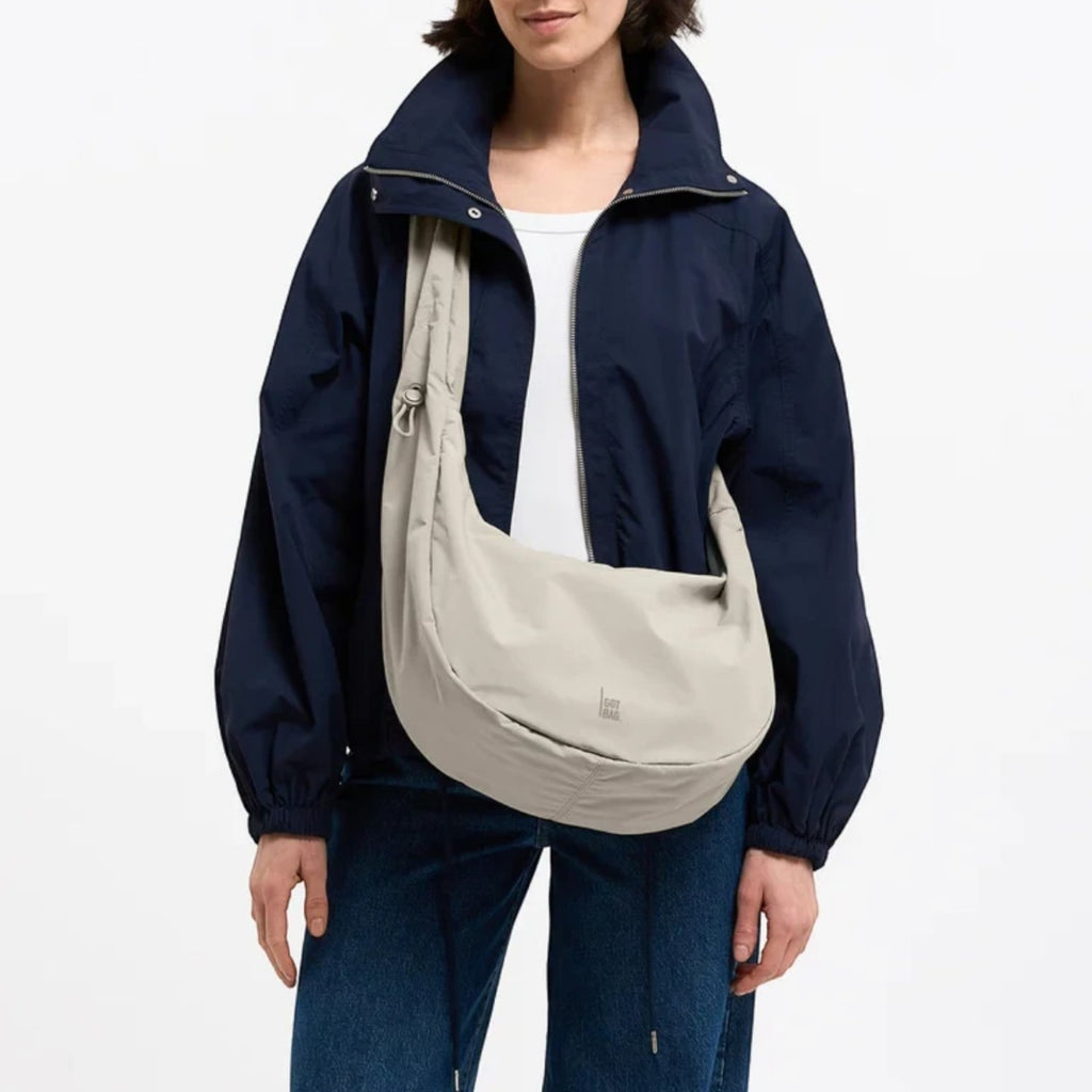 Lieblingstasche Moon Bag Ruffle Large in beige, worn as a crossbody bag by a model in a navy jacket.
