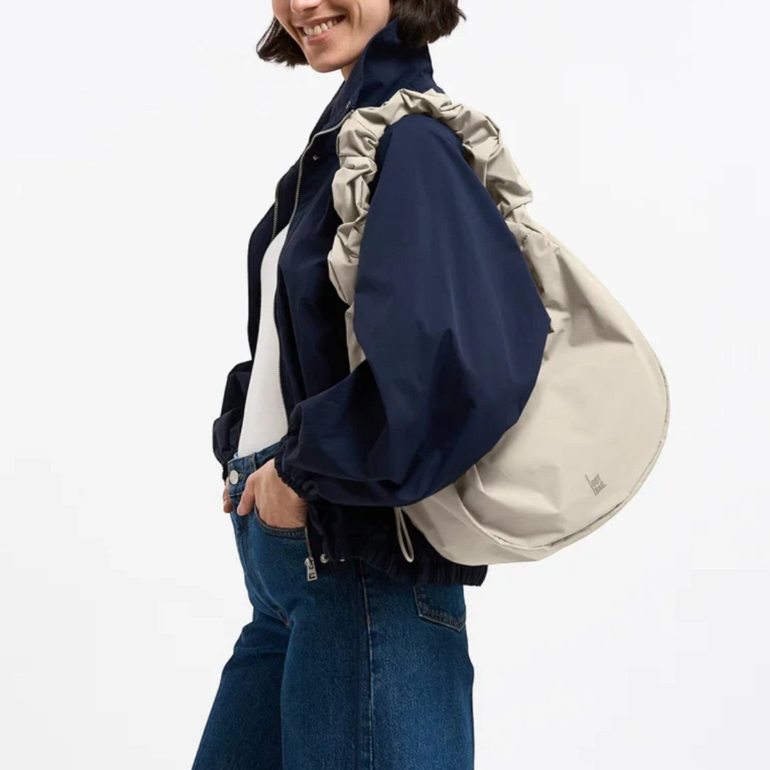 Lieblingstasche Moon Bag Ruffle Large in beige, worn as a shoulder bag by a woman in a navy jacket and jeans.