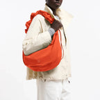 Lieblingstasche Moon Bag Ruffle Large in bright orange, worn as a shoulder bag by a model in a light jacket.