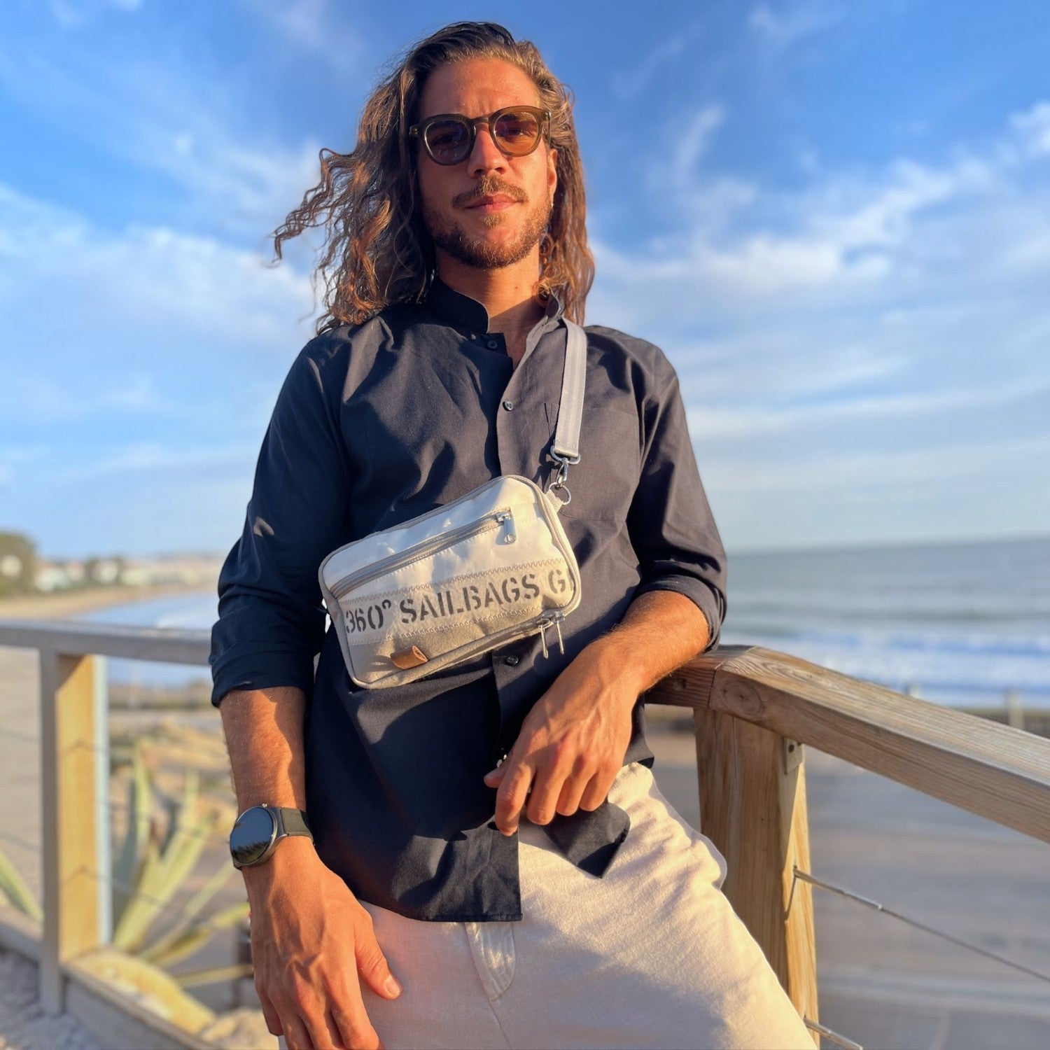 Lieblingstasche Nautik crossbody bag in white sailcloth worn by a man on a coastal boardwalk at sunset
