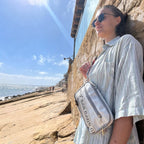Lieblingstasche Nautik white sailcloth crossbody bag worn by a woman against a stone wall by the ocean