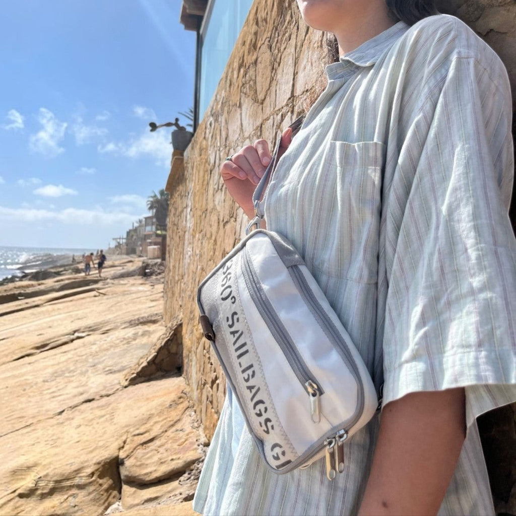 Lieblingstasche Nautik white sailcloth crossbody bag worn by a woman against a stone wall by the ocean