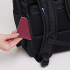 Lieblingstasche Pro Pack black backpack showing a hidden zippered back pocket with a passport being inserted.