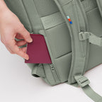 Lieblingstasche Pro Pack sage green backpack with a hand placing a passport into the hidden back security pocket