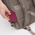 Lieblingstasche Pro Pack backpack in taupe with a hand inserting a passport into a side pocket.