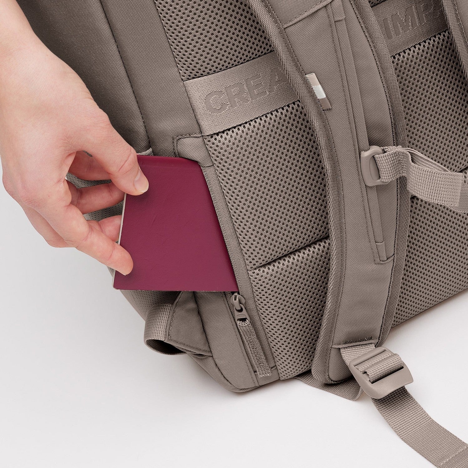 Lieblingstasche Pro Pack backpack in taupe with a hand inserting a passport into a side pocket.