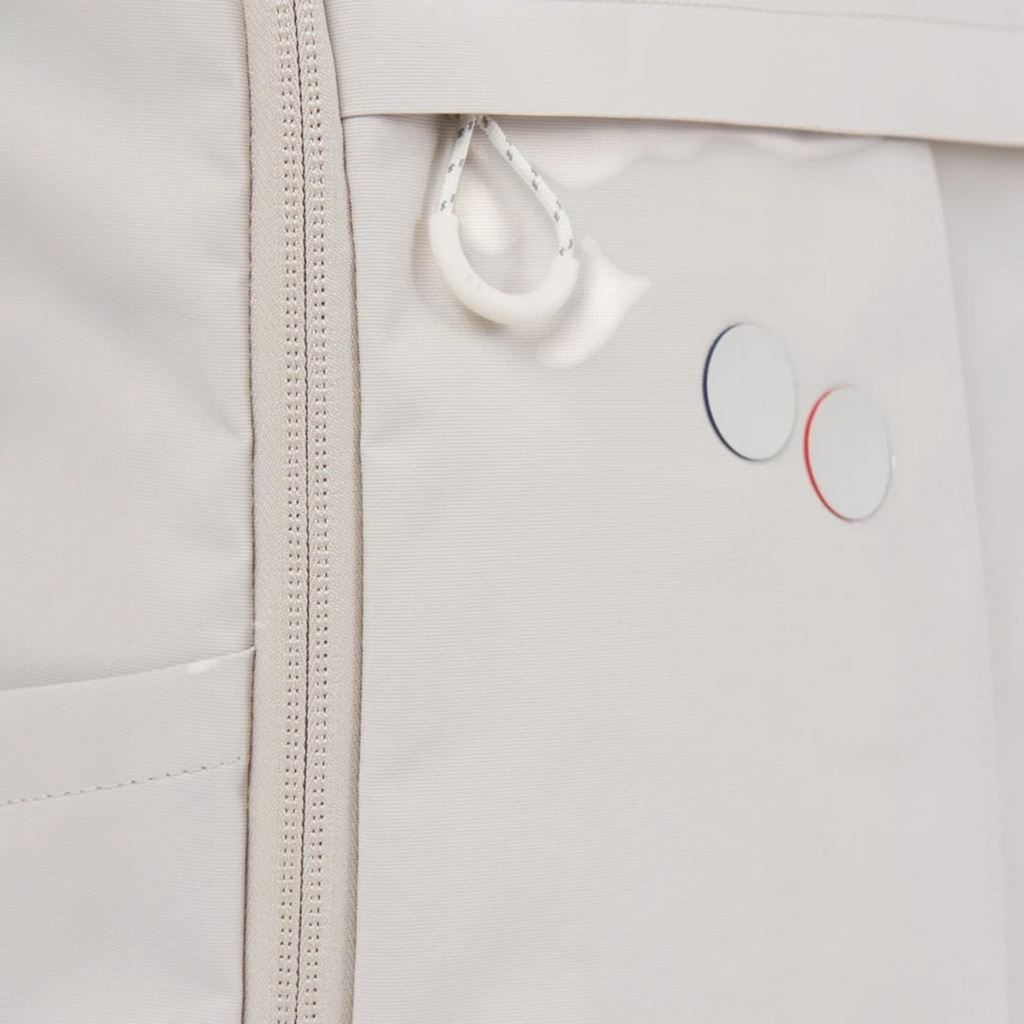 Close-up of a beige Lieblingstasche Purik backpack featuring a zipper, white cord pull, and circular logo detail.