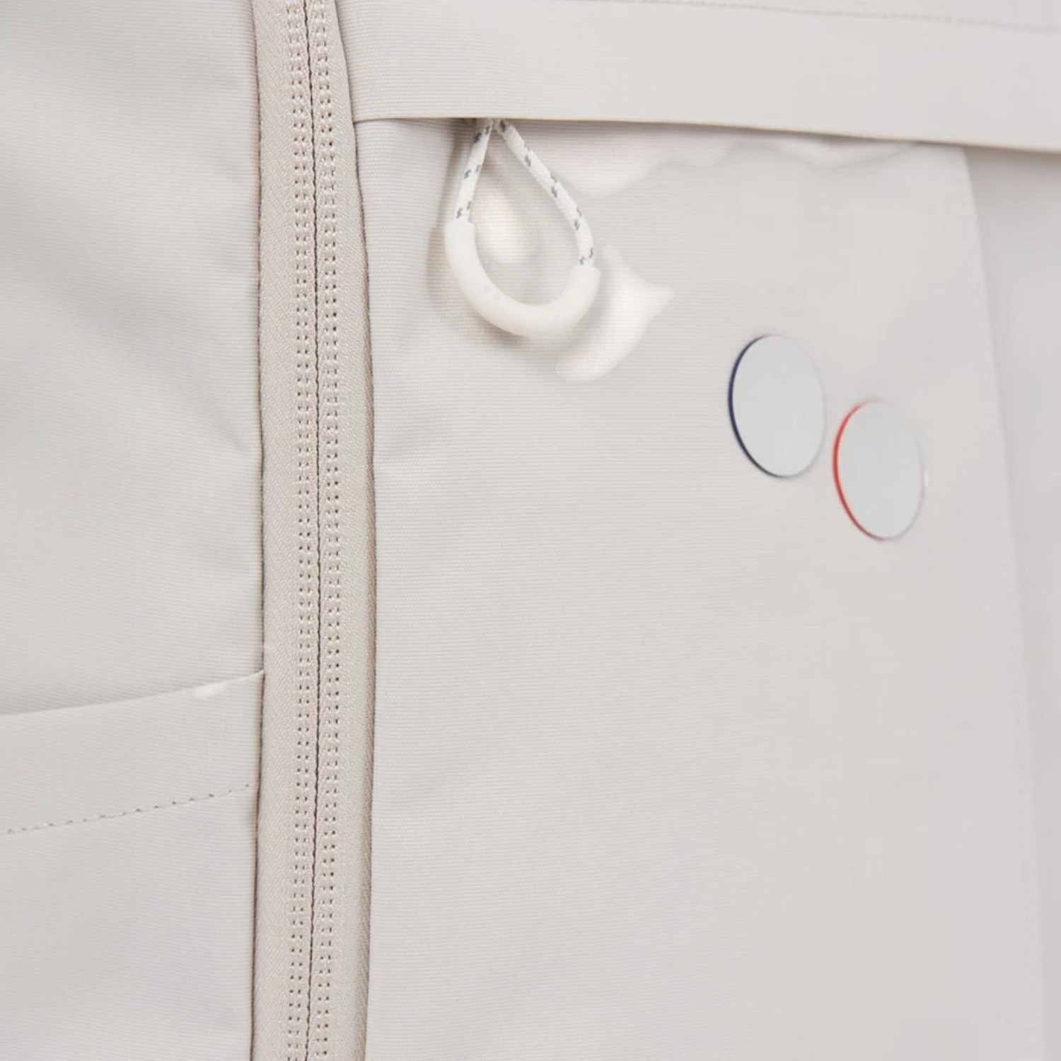 Close-up of a beige Lieblingstasche Purik backpack featuring a zipper, white cord pull, and circular logo detail.
