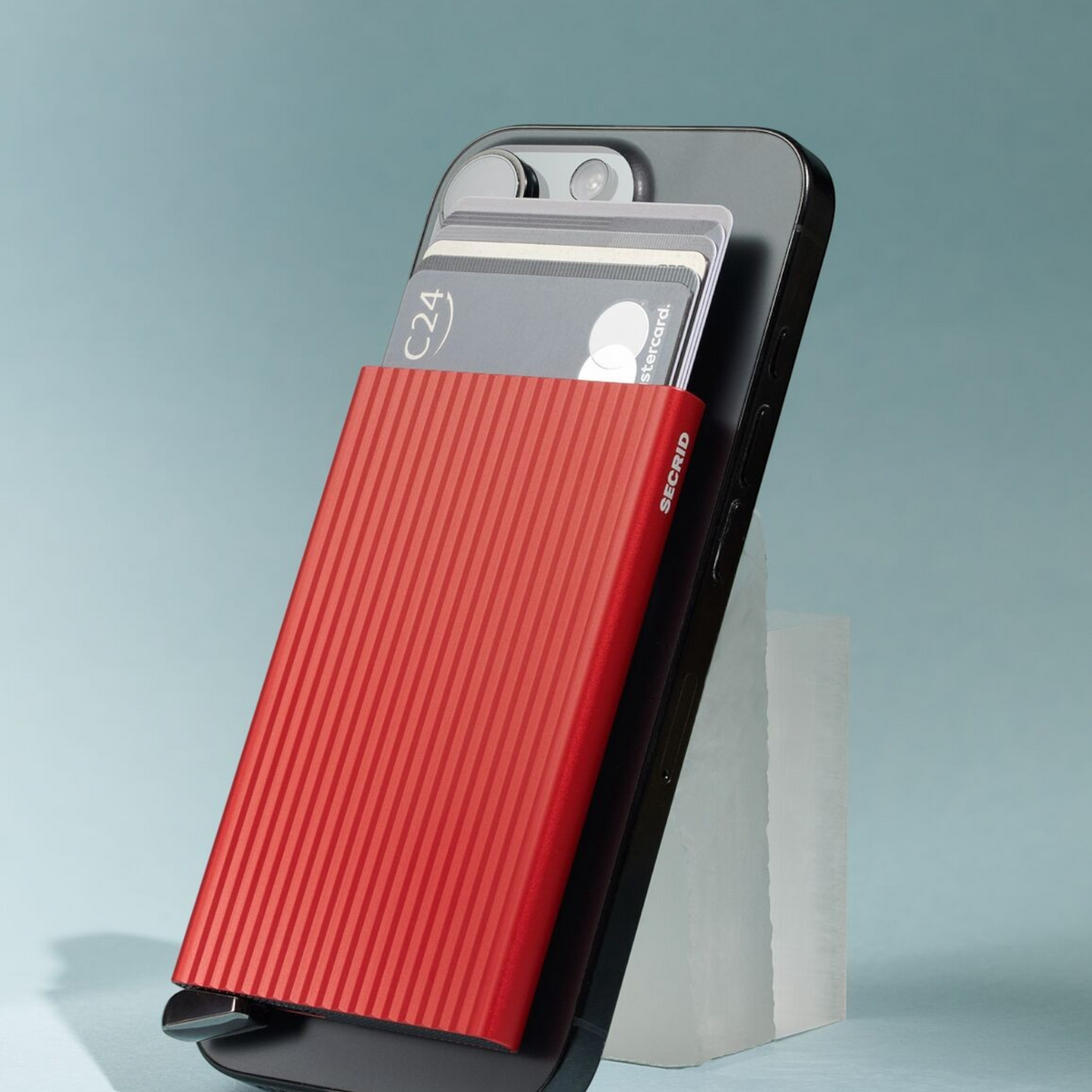 Lieblingstasche red fluted MagSafe card protector attached to the back of a black smartphone with credit cards inside.