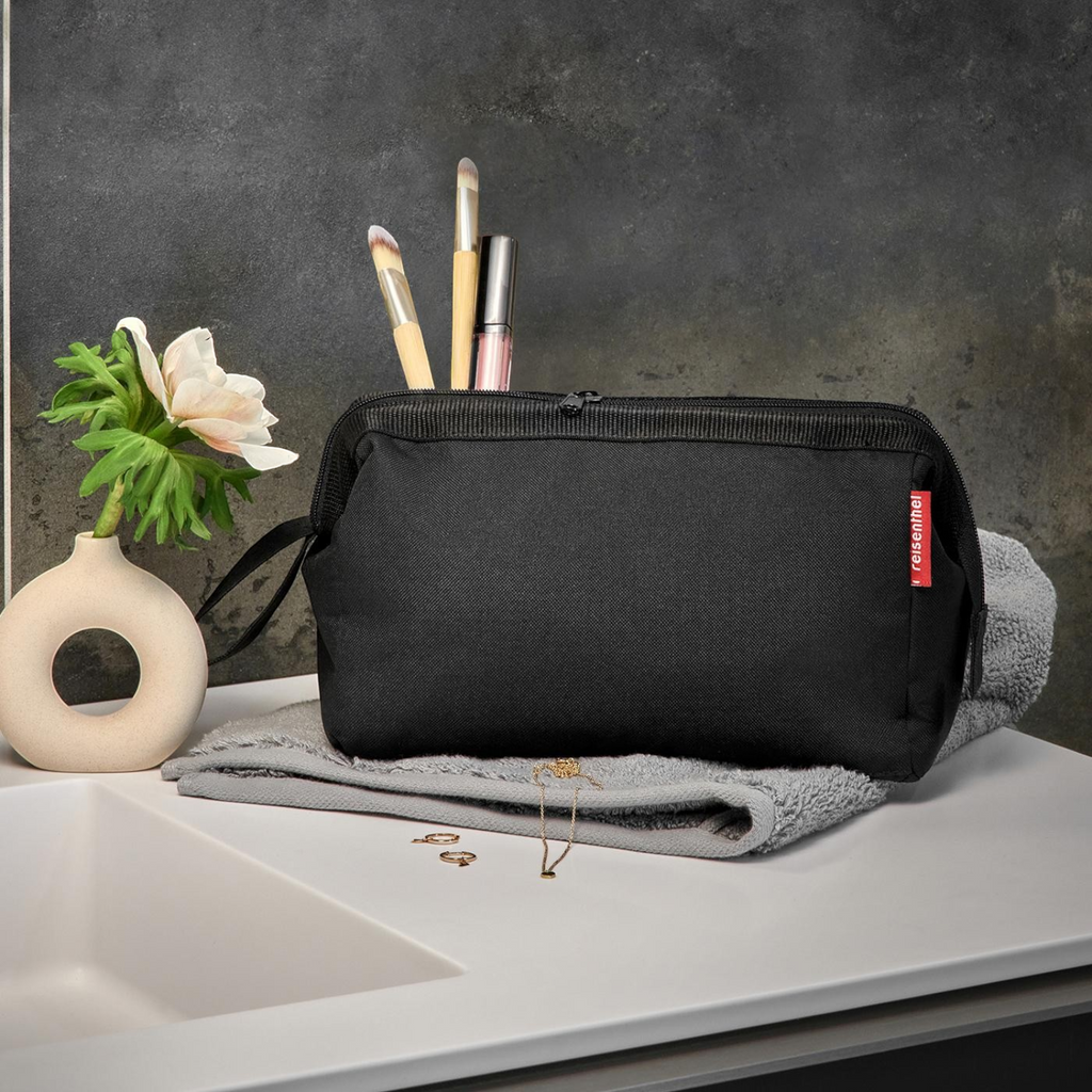 Lieblingstasche reisenthel Travelcosmetic black toiletry bag with metal frame opening on a bathroom counter