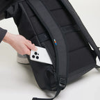 Lieblingstasche Rolltop Easy black backpack with a hand placing a smartphone into the side zipper pocket