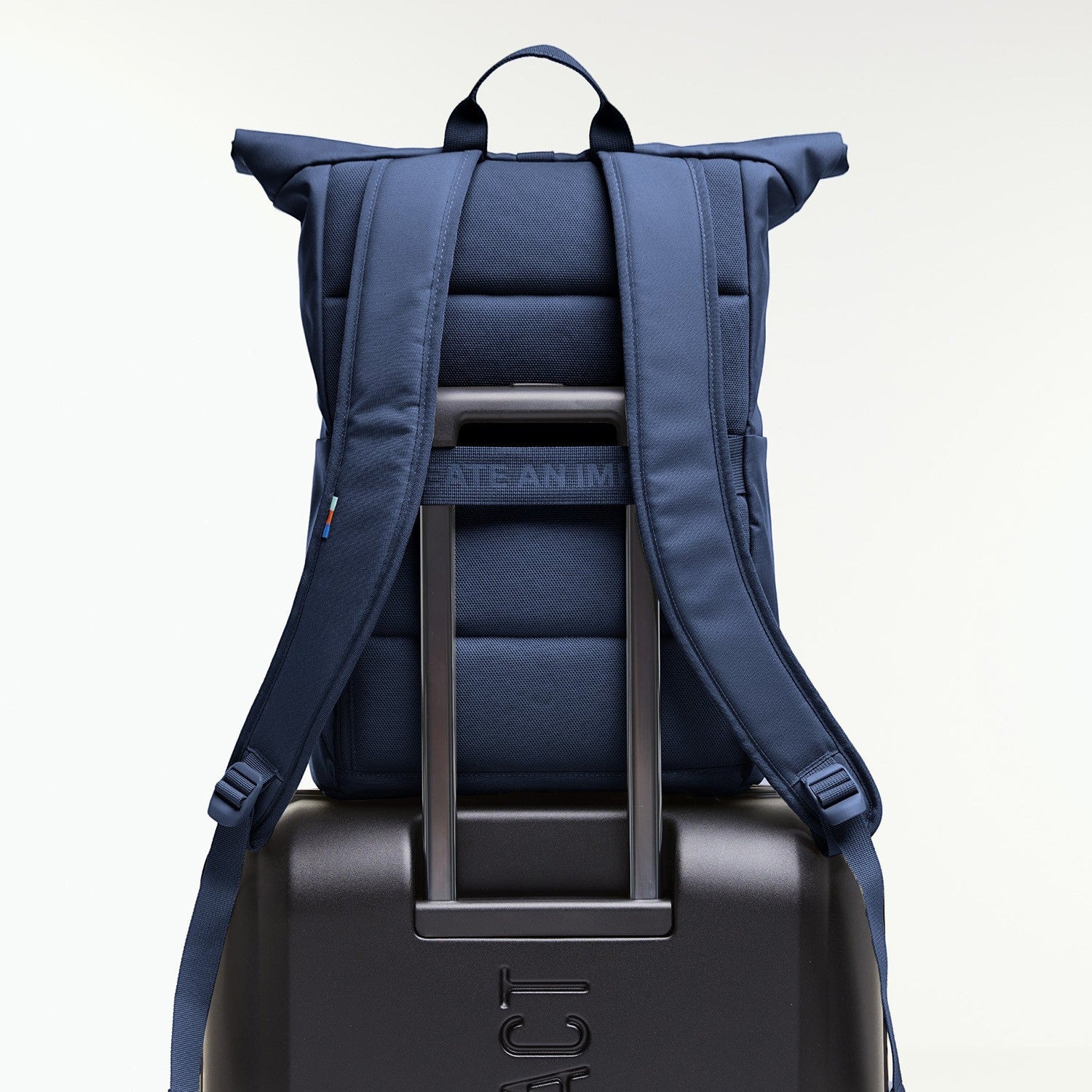 Lieblingstasche Rolltop Easy navy blue backpack with padded straps, attached to a black suitcase.