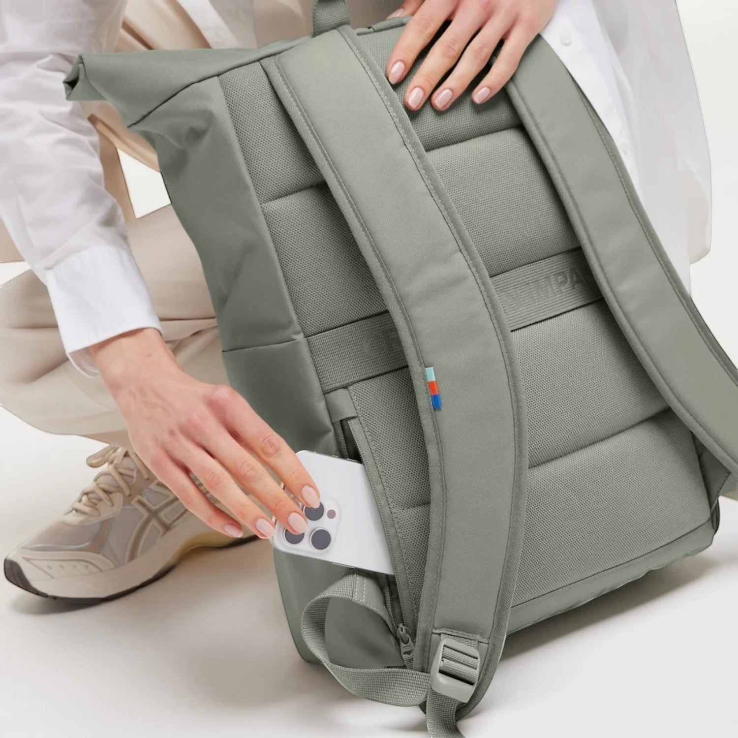 Lieblingstasche Rolltop Easy backpack in sage green with a person placing a smartphone into the back zipper pocket.