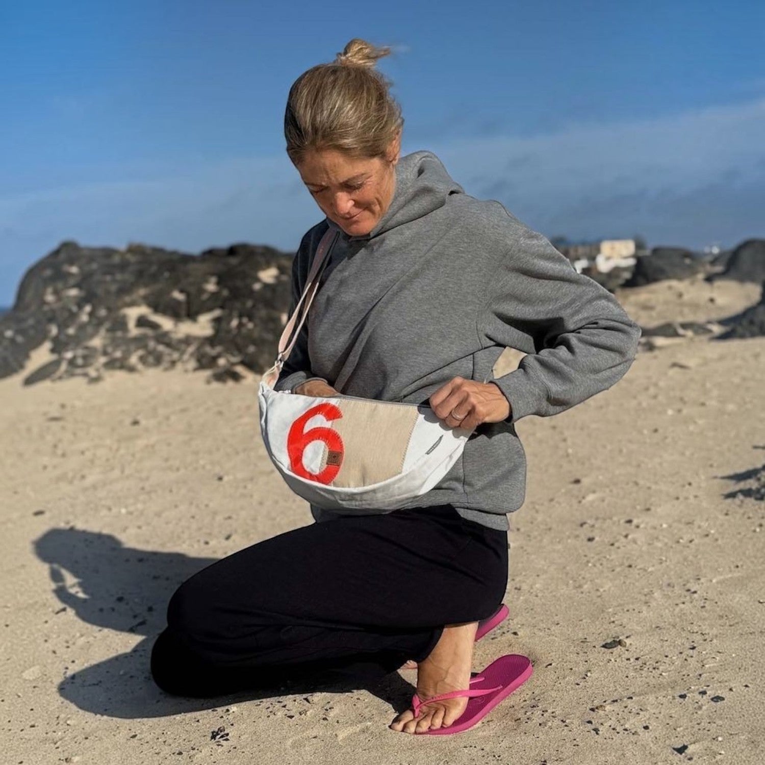 Lieblingstasche Roop waist bag in white canvas with red number 6 detail, worn by a woman on a sandy beach.