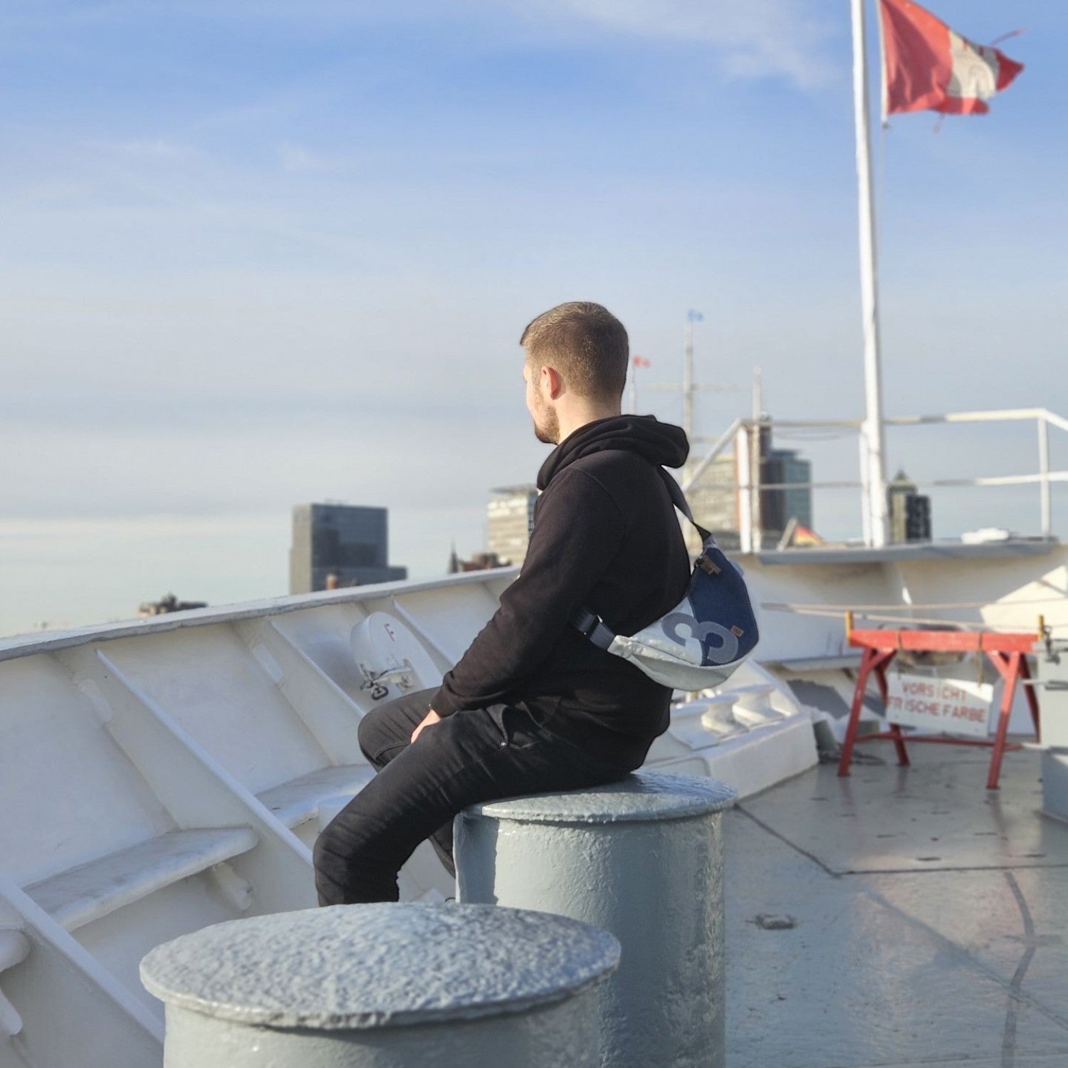 Lieblingstasche Roop moonbag made from recycled white and blue sailcloth worn by a man on a ship deck