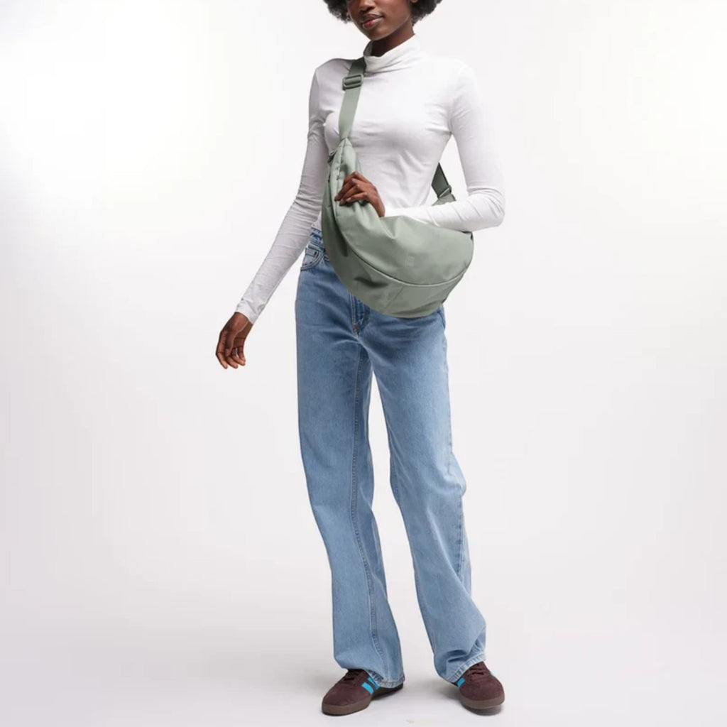 Model wearing a sage green GOT BAG Moon Bag Large crossbody, styled with a white turtleneck and blue jeans.